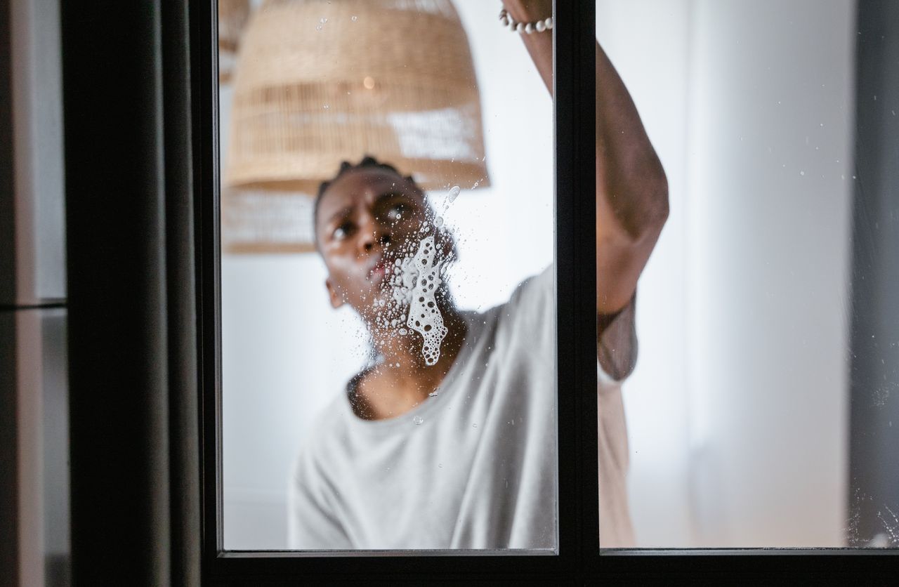 Un homme adulte nettoie une fenêtre en verre à l’intérieur, mettant l’accent sur les tâches ménagères et la propreté.